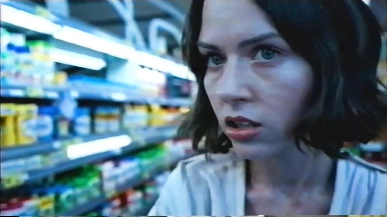 A short-haired subject with a comparatively human facial profile beside shelves of packaged goods, shortly before the canine muzzle shown in the next sequence.