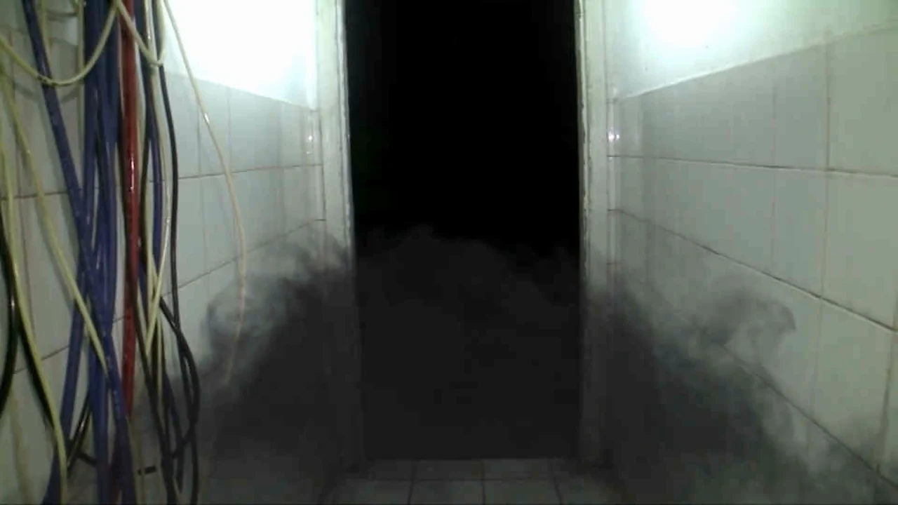 An unlit doorway at the end of a narrow tiled passage, with exposed cables and dark wisps near the floor.